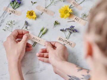Hands arranging flowers with positive words on a marble surface. Ideal for art and inspiration themes.