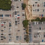 Aerial drone shot of urban parking lot filled with parked cars, showcasing urban infrastructure.