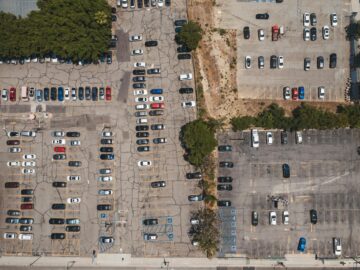 Aerial drone shot of urban parking lot filled with parked cars, showcasing urban infrastructure.