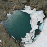 Explore the striking aerial view of a frozen glacier lake in Binn, Switzerland, surrounded by rugged rock formations.