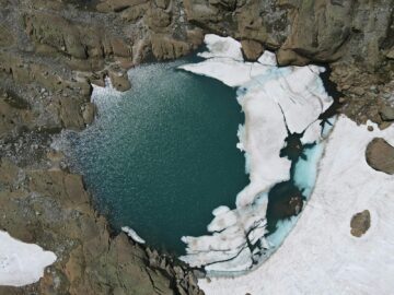 Explore the striking aerial view of a frozen glacier lake in Binn, Switzerland, surrounded by rugged rock formations.