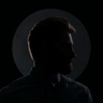 Moody silhouette profile of a man against a dark background with a circular spotlight.