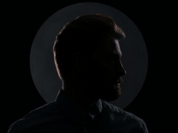 Moody silhouette profile of a man against a dark background with a circular spotlight.