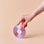 A hand gently holds a shiny compact disc against a neutral background.