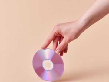 A hand gently holds a shiny compact disc against a neutral background.