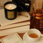 A warm and cozy reading corner with books, candle, coffee, and vintage camera on display.