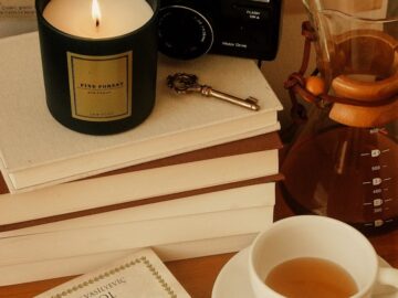 A warm and cozy reading corner with books, candle, coffee, and vintage camera on display.