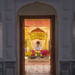 A view into an ornate Sikh temple through an open door, focusing on the altar and religious symbols.