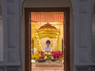 A view into an ornate Sikh temple through an open door, focusing on the altar and religious symbols.
