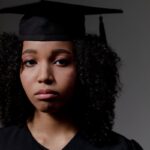 Solemn expression of a young graduate wearing cap and gown indoors.