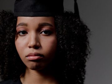 Solemn expression of a young graduate wearing cap and gown indoors.