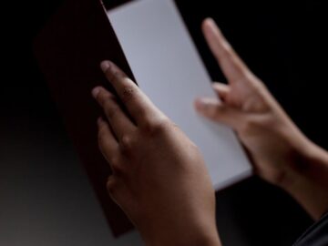 Unrecognizable person holding a diploma against a black background, symbolizing achievement and education.