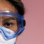 Detailed close-up of a woman wearing safety goggles and a mask against a soft pink background.