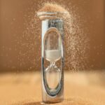 Close-up of an hourglass with sand falling, capturing the essence of time against a yellow background.