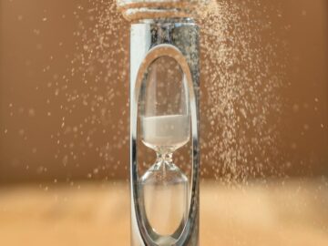 Close-up of an hourglass with sand falling, capturing the essence of time against a yellow background.