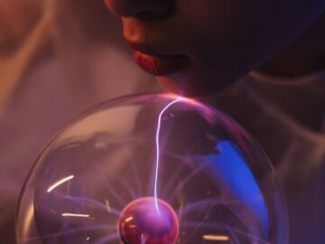 Close-up of woman interacting with a glowing plasma globe, showcasing electricity patterns.