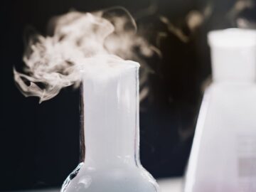 Steam rising from colorful liquid in glass flasks during a lab experiment.