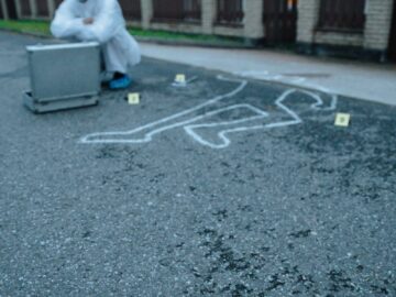 A forensic investigator examines a crime scene with evidence markers on a street.
