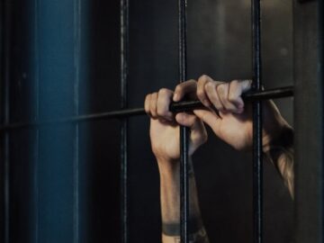 Close-up of hands holding metal prison bars, illustrating confinement and punishment.