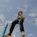 Teen balancing on monkey bars, capturing adventurous spirit under a clear blue sky.