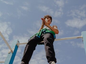 Teen balancing on monkey bars, capturing adventurous spirit under a clear blue sky.