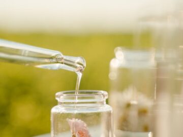 Close-up of a pipette adding liquid to a jar with a flower, outdoors in daylight.