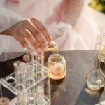 A woman in a pink dress pours liquid into a jar outdoors, surrounded by test tubes.