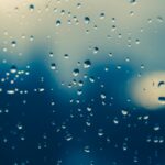 Close-up of raindrops on a window, creating a moody, blurred view outside.