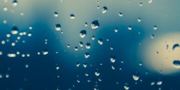 Close-up of raindrops on a window, creating a moody, blurred view outside.