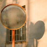 Abstract urban scene with reflections in a convex mirror and building shadows on a sunny day.