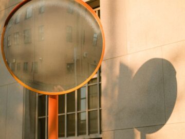 Abstract urban scene with reflections in a convex mirror and building shadows on a sunny day.
