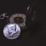 Close-up of a vintage silver coin with a pocket watch, symbolizing time and wealth.