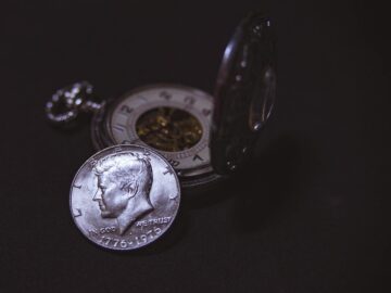Close-up of a vintage silver coin with a pocket watch, symbolizing time and wealth.