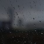 Raindrops on glass with a blurred cityscape in the background, creating a moody atmosphere.