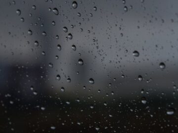 Raindrops on glass with a blurred cityscape in the background, creating a moody atmosphere.