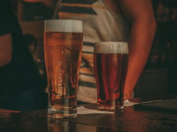 Close-up of two pints of beer on a bar counter in a lively pub setting.