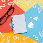 Flat lay of a colorful desktop featuring a notebook, eyeglasses, and house key with numbers scattered.