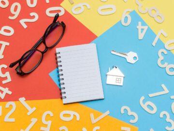 Flat lay of a colorful desktop featuring a notebook, eyeglasses, and house key with numbers scattered.