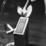 A dramatic black and white image capturing a matchstick burst into flames with smoky aura.