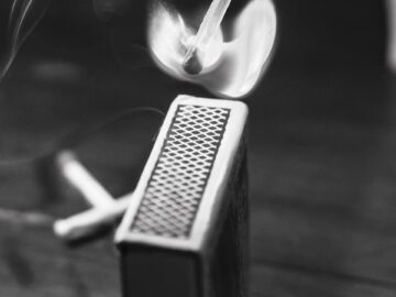 A dramatic black and white image capturing a matchstick burst into flames with smoky aura.