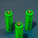 Close-up of three green rechargeable batteries standing on a blue surface.