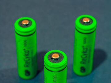 Close-up of three green rechargeable batteries standing on a blue surface.