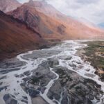 A breathtaking aerial view of river patterns cutting through Spiti Valley's mountainous terrain under a cloudy sky.