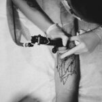 A tattoo artist skillfully designs a unique pattern on a client's arm in monochrome.