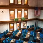 An interior view of the Indiana Senate Chamber featuring desks and the American flag.