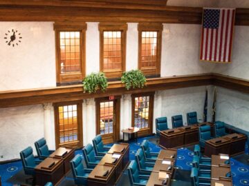 An interior view of the Indiana Senate Chamber featuring desks and the American flag.