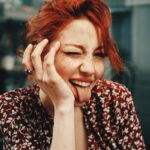 A cheerful woman with red hair making a playful face indoors.