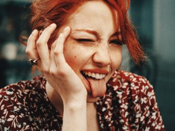 A cheerful woman with red hair making a playful face indoors.