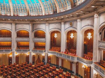 Majestic view of an ornate parliamentary chamber with a striking turquoise dome and plush seating.