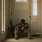 A solitary soldier in uniform sitting by a door, reflecting mood.